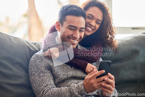 Image of Happy couple, phone and sofa laughing for social media, internet meme or online streaming service at home. Young interracial woman and man or partner on website, connection and hug or love on couch