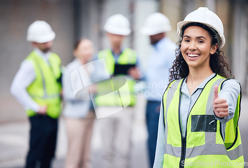 Image of Thumbs up, woman construction worker and at a industrial workplace happy with her colleagues in the background. Thank you or success, agreement and cheerful or excited architect at building site