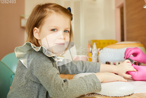 Image of Little girl in nail salon receiving manicure by beautician. Little girl getting manicure at beauty salon.