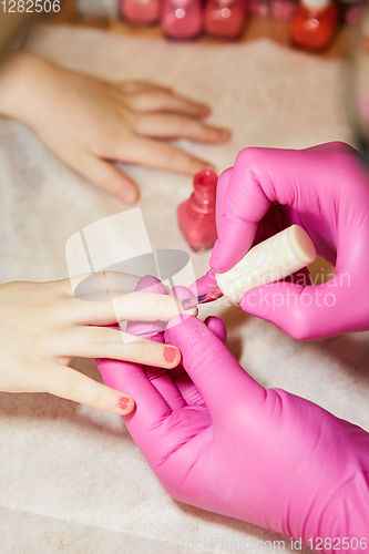 Image of Little girl is getting manicure in beauty salon, close-up.