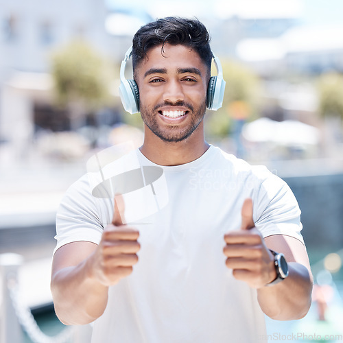 Image of Happy man, headphones and listening to music with thumbs up for winning, fitness or success in city. Portrait of male person, athlete or runner with headset, thumb emoji or yes sign for audio track