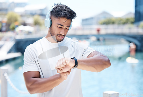 Image of Fitness, music and man in city with smart watch for running, exercise and tracking workout. Headphones, sports and male person check wristband for marathon training, wellness and performance time