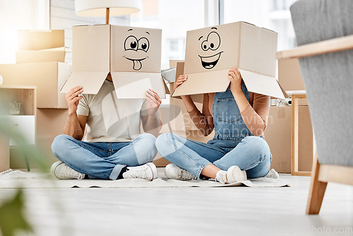 Image of Funny, couple moving and boxes on head with faces, smile or emoji drawing on cardboard and new house, property or real estate. People, comic and box on body with happiness, crazy or joke in home
