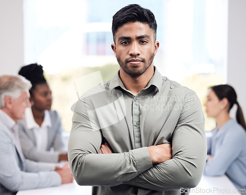 Image of Portrait, serious and a business man arms crossed in the boardroom with his team planning in the background. Leadership, workshop and focus with a confident young male employee standing in the office