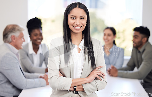 Image of Portrait, happy and a business woman arms crossed in a boardroom with her team planning in the background. Leadership, workshop and smile with a confident young female employee standing in the office