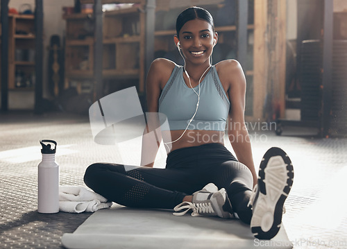 Image of Woman in gym, relax on mat with fitness and smile, workout with earphones, portrait and sports. Healthy, active with happy Indian female sitting in studio exercise with music, health and wellness