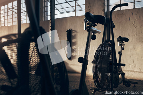 Image of Spinning bike, empty and gym for exercise with a shadow background at a warehouse with light. Club, cardio bicycle for fitness equipment for training and workout in storage venue in the dark.