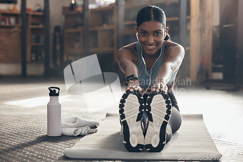 Image of Woman is stretching legs in gym, fitness and smile, start workout with earphones, portrait and sport preparation. Health, active with happy Indian female warm up and ready for exercise with music