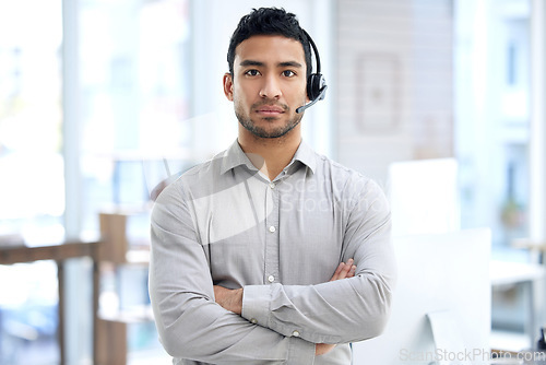 Image of Call center, man and portrait with arms crossed in office, telemarketing or serious face for crm job. Young indian consultant, voip headset and customer service for advice, sales or technical support