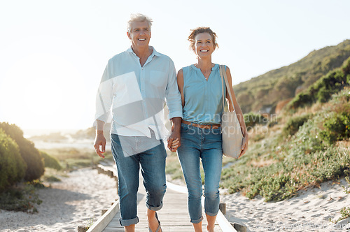 Image of Senior, couple and walking at the beach with hands in portrait for happiness on a vacation in the outdoor. Mature, woman and man holding by ocean for travel on holiday with sunshine for the weekend.