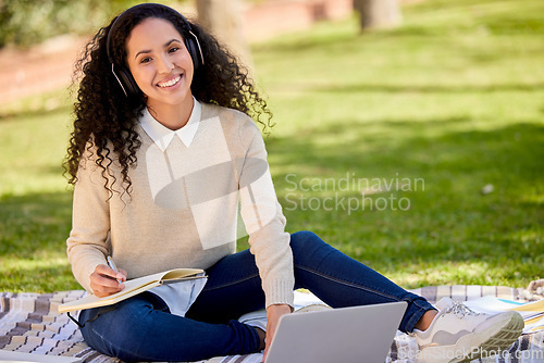 Image of Portrait of happy woman in park studying with headphones, laptop and notes for education in nature, learning and music. Smile, research and university student on grass with audio books for project.