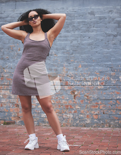 Image of Fashion, young woman and posing near a wall outside or lady with attitude feeling freedom or happy with sunglasses in city. Urban fashion, cool eyewear and female model with afro or stylish clothing