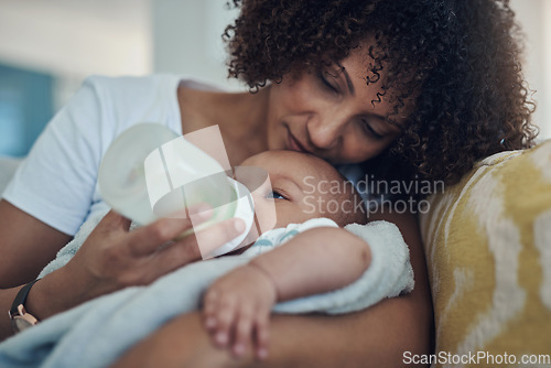Image of Care, woman feeding her baby with bottle and in living room on the sofa at their home. Family love, drinking or nutrition and black mother feed her newborn child on couch of their house with formula