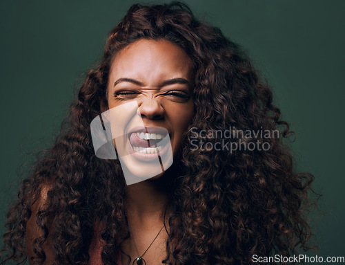 Image of Tongue out, portrait and young woman in studio with natural curly hair, happy meme or wink on a green background. Face, crazy and female model with funny personality, goofy and silly emoji expression