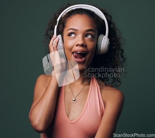 Image of Music, headphones and gen z girl in studio for streaming, silly face or audio on green background. Podcast and goofy female model relax while listening to radio, audio or online playlist