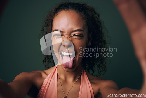 Image of Selfie, tongue out and young woman in studio with facial, expression or personality on green background. Face, emoji and crazy gen z model wink for silly profile picture, portrait or fun goofy post