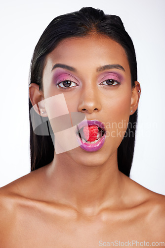 Image of Woman, makeup and raspberry in mouth for studio portrait, glow color and skincare by white background. Face of indian model eating fruits with bold cosmetics, facial aesthetic and shine for beauty