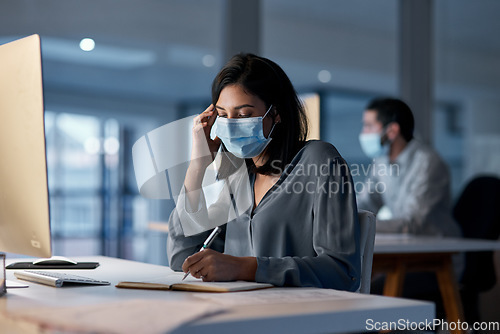 Image of Call center, woman and notebook at computer with mask for customer support, sales and CRM consulting at night. Female agent, telemarketing and virus protection on face in office for administration