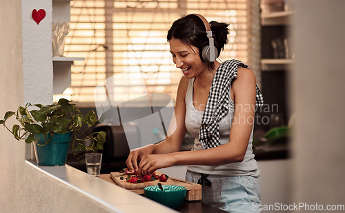 Image of Music headphones, morning and woman cooking breakfast of healthy strawberry food at home. Kitchen, headphone and happy female person making snack with fruits while listening to audio, sound and radio