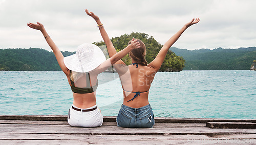 Image of Rear view, people sitting on a jetty and carefree for excitement outdoors by the ocean. Summer vacation or holiday break, freedom and excited or cheerful women sit on pier at sea for fresh air