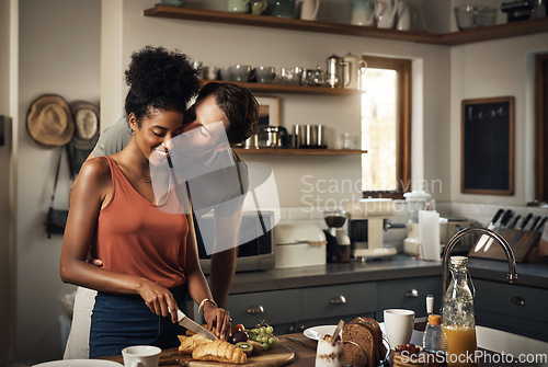 Image of Interracial couple, kiss and cooking in kitchen for morning breakfast, love or caring relationship at home. Man kissing woman while making food, romantic meal or cutting ingredients on table in house