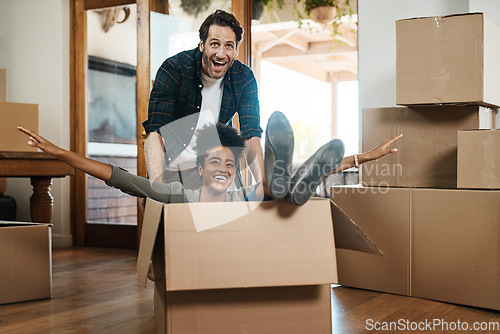 Image of Happy couple, box and real estate in new home or property for renovation and investment together. Excited interracial man, woman and playing in boxes, moving to house or celebration of fun relocation