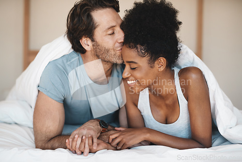 Image of Happy interracial couple, bed and morning kiss in relax or bonding relationship at home. Man kissing woman on forehead in happiness or embrace for love or relaxing weekend together in the bedroom