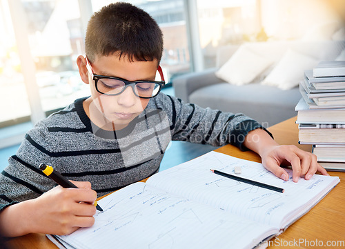 Image of Boy child, student and writing in book for studying, education and learning homework on table at home. Smart little kid busy with mathematics, textbooks and problem solving for study in living room