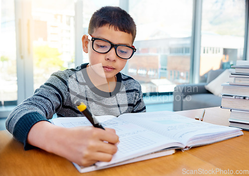 Image of Boy, student and writing in book for studying, homework or learning in education on table at home. Smart little kid or child busy on mathematics, textbooks or problem solving for study in living room