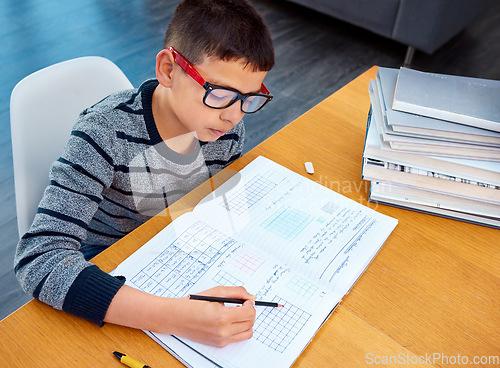 Image of Boy, student and writing in book for math, studying or homework for learning, assessment or education on table. Smart kid, young child and busy reading mathematics textbook, problem solving and focus