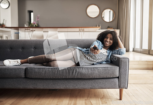 Image of Sofa, African woman watching tv and with remote on the couch in living room of her home. Entertainment or relax, happiness and comfortable black female person streaming series or a movie in free time
