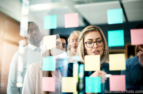 Image of Manager, sticky note and brainstorming with team on glass for schedule, calendar and planning goals, agenda and timeline. Woman, mentor and collaboration of ideas at window for feedback in office