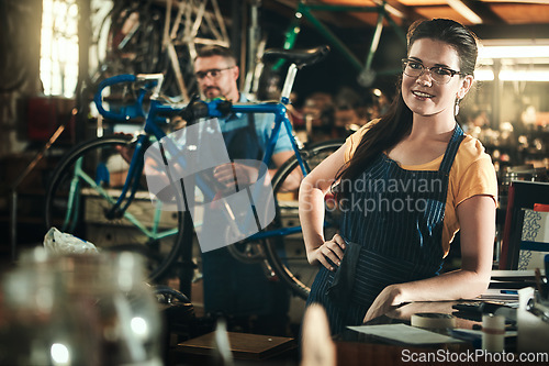 Image of Portrait, working and smile of woman in bicycle shop, repair store or cycling workshop. Face, bike mechanic and confident person, professional or technician standing with glasses in small business.