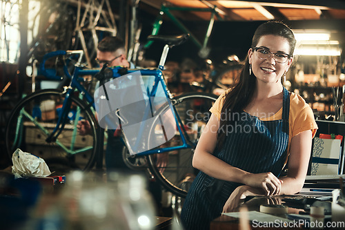 Image of Portrait, mechanic and smile of woman in bicycle shop, repair store or cycling workshop. Face, bike technician and confident female person, business owner and professional standing with glasses.