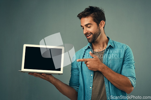 Image of Happy man, laptop and pointing to mockup screen for advertising or marketing against a grey studio background. Male person smiling and showing technology display or mock up space for advertisement