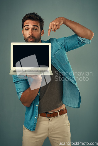 Image of Man, laptop and pointing on mockup screen for advertising or marketing against a grey studio background. Portrait of a male person showing computer display, mock up and tech space for advertisement