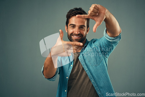 Image of Frame, hands and face portrait of man in studio on gray background with happiness, confident and smile. Photographer, happy and male person with hand sign for picture, photography and finger border