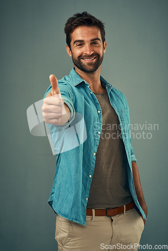 Image of Happy man, portrait and thumbs up for winning, success or good job against a grey studio background. Male person with smile showing thumb emoji, yes sign or like for approval, thank you or support