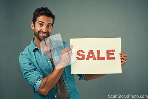 Image of Happy man, portrait and sale sign for advertising, marketing or branding against a grey studio background. Male person or realtor holding billboard or poster with smile for selling advertisement