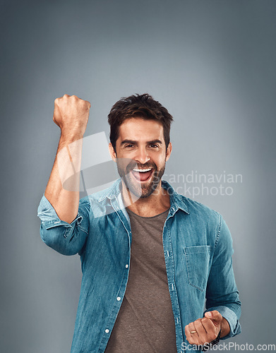 Image of Happy man, fist and celebration for winning, success or victory against a grey studio background. Excited portrait of male person or winner in achievement, win or accomplishment on mockup space