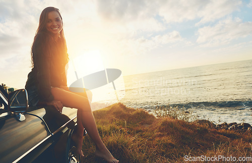 Image of Road trip, portrait and sunset with a woman at the ocean, sitting on her car bonnet during travel for freedom or escape. Nature, flare and mockup with a young female tourist traveling in summer