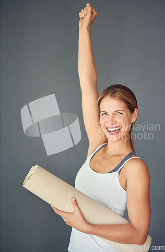 Image of Happy woman, portrait and yoga mat with fist in celebration for healthy exercise against a grey studio background. Excited female person or yogi with smile for winning, fitness or workout success