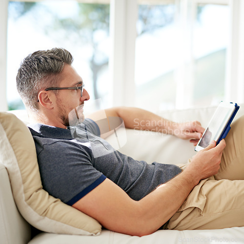 Image of Man, relax and tablet on living room sofa, reading and social media for video, game or movies in home. Mature guy, digital touchscreen and lounge couch for internet blog, news and web app in house