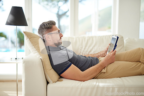 Image of Man, relax and tablet on living room couch, reading and social media for video, game or movies in home. Mature guy, digital touchscreen and lounge sofa for internet blog, news or web app in house