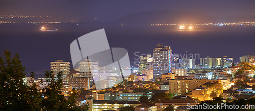 Image of Harbour, buildings and city at night with lights, urban development and streets. Dark, travel and outdoor residential architecture of downtown with ocean or sea water in the evening with a skyline.