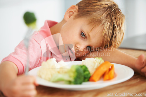 Image of Sad, healthy and a child with vegetables for dinner, unhappy and problem with food. Frustrated, hungry and a little boy eating broccoli and carrots, disappointed with lunch and nutrition for youth