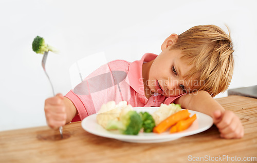 Image of Sad, diet and a child with vegetables for dinner, unhappy meal and problem with food. Frustrated, hungry and dislike of boy kid eating broccoli, carrots and disappointed with healthy lunch at home