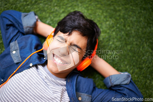 Image of Boy child, lawn and lying with headphones, free or excited for music, streaming or online audio in top view. Male kid, happiness and listen to sound, internet radio or podcast on grass in garden