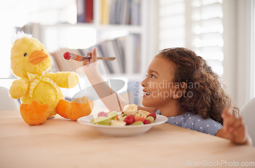 Image of Child feeding, teddy bear and food at home with happiness and wellness meal with a smile. House, nutrition and young girl with healthy fruit salad and fruits of a hungry kid with toy duck at a table