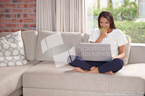 Image of Laptop, eating apple and a woman on a home sofa with internet for streaming, remote work and reading blog online. Happy female person relax on couch with fruit, snack and computer for elearning tech